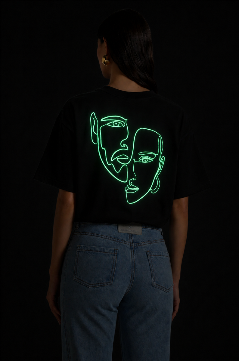 Femme portant un t-shirt oversize noir Rich.Art avec illustration artistique néon verte représentant deux visages abstraits au dos
